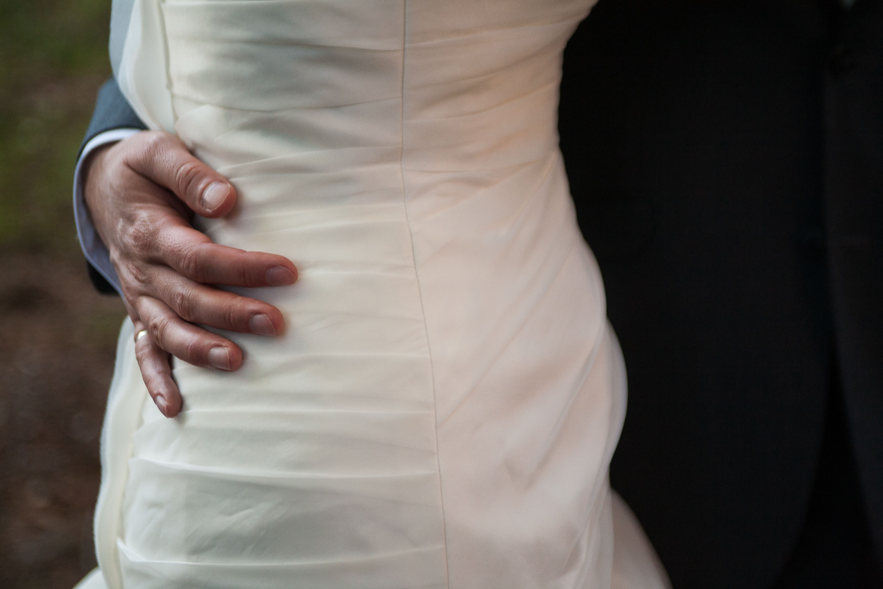 The groom's hand embracing the bride's waist, with a close up of her Vera Wang gown, at Pema Osel Ling in the Santa Cruz mountains