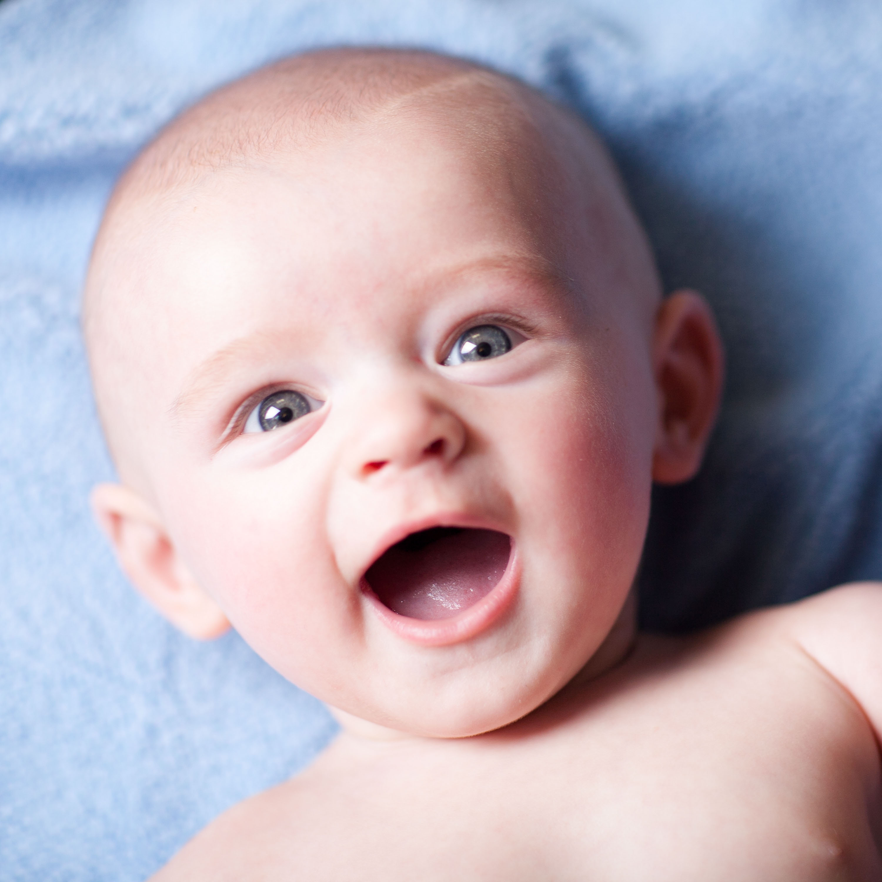 A super smiley blue-eyed baby on a blue blanket in the studio.