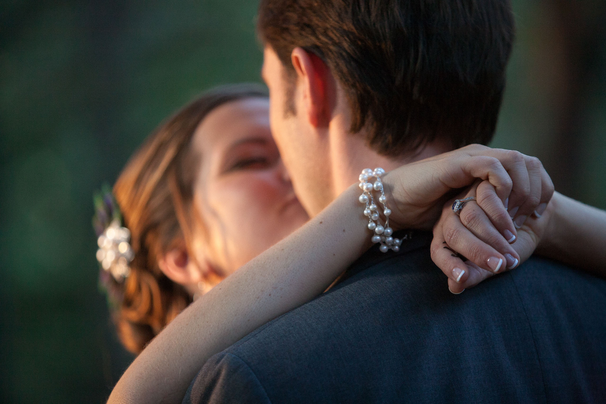 A romantic kiss showing a closeup of the bride's pearls and wedding ring