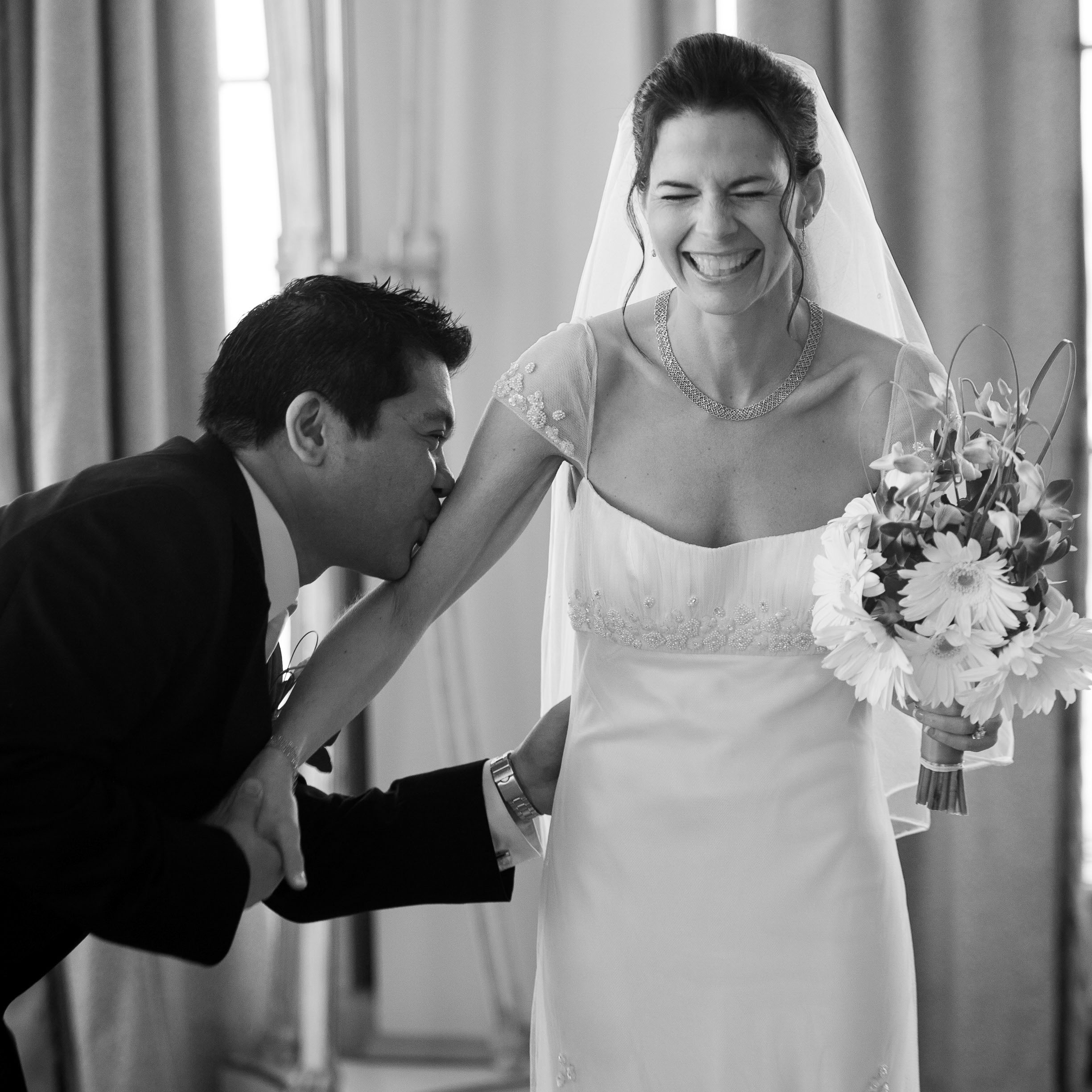 A beautiful bride laughs as her husband plants kisses along her arm,  at the St. Francis Hotel in San Francisco