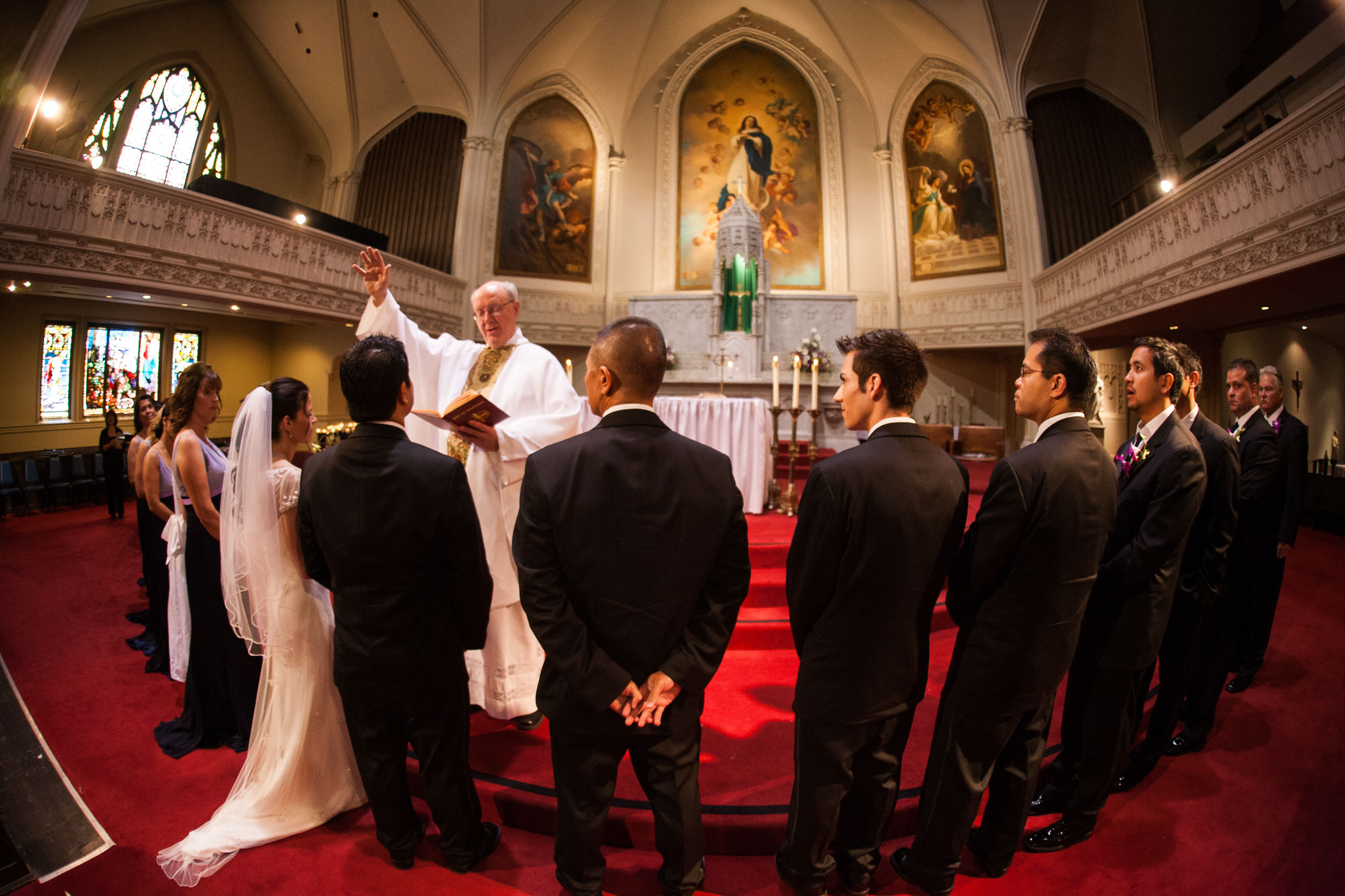 The pastor blesses the bride and groom while the entire wedding party looks on,  at Old St. Mary's Church in San Francisco