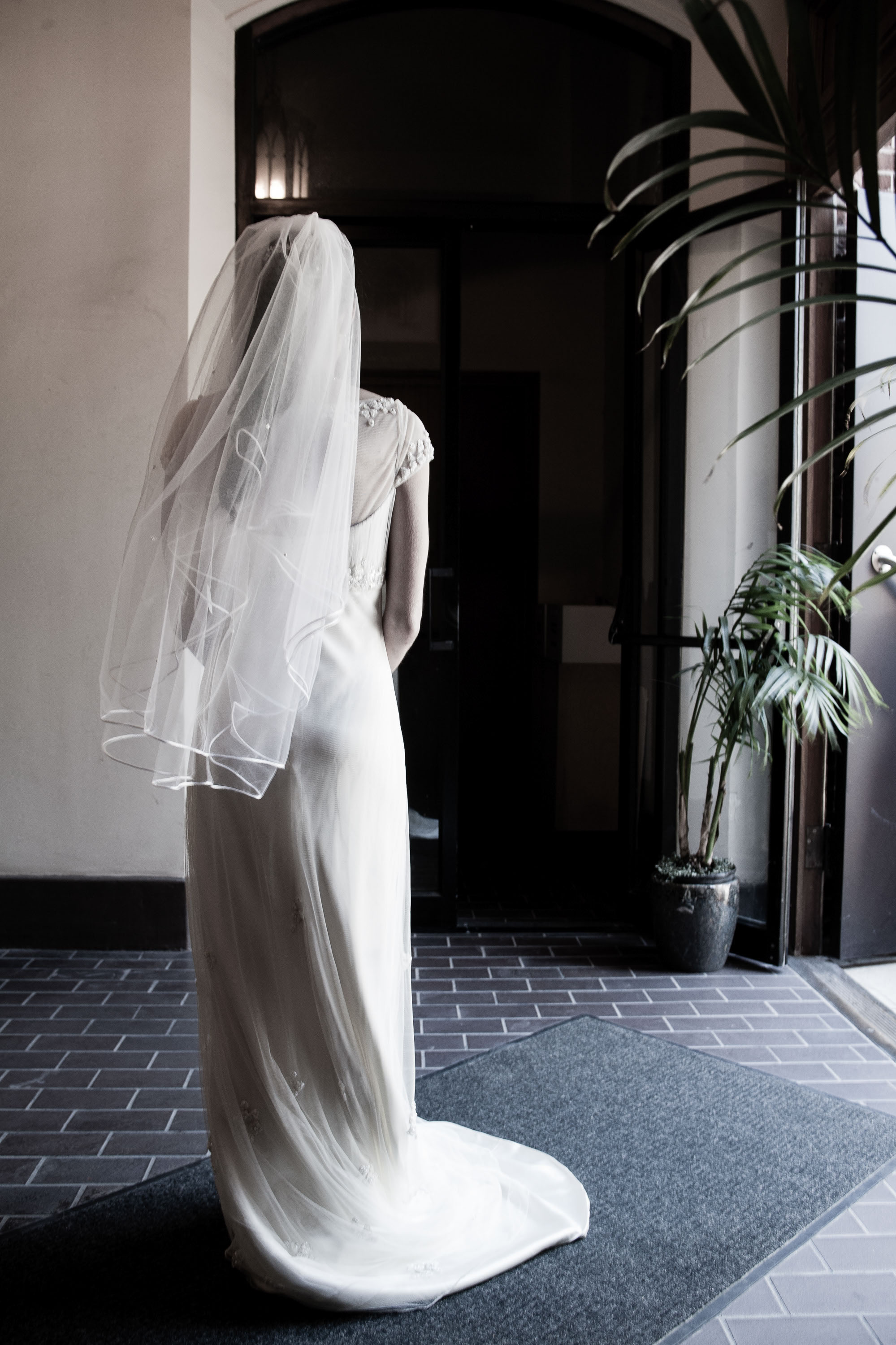 The elegant currve of the bride's dress lit from the doorway  at Old St. Mary's Church in San Francisco