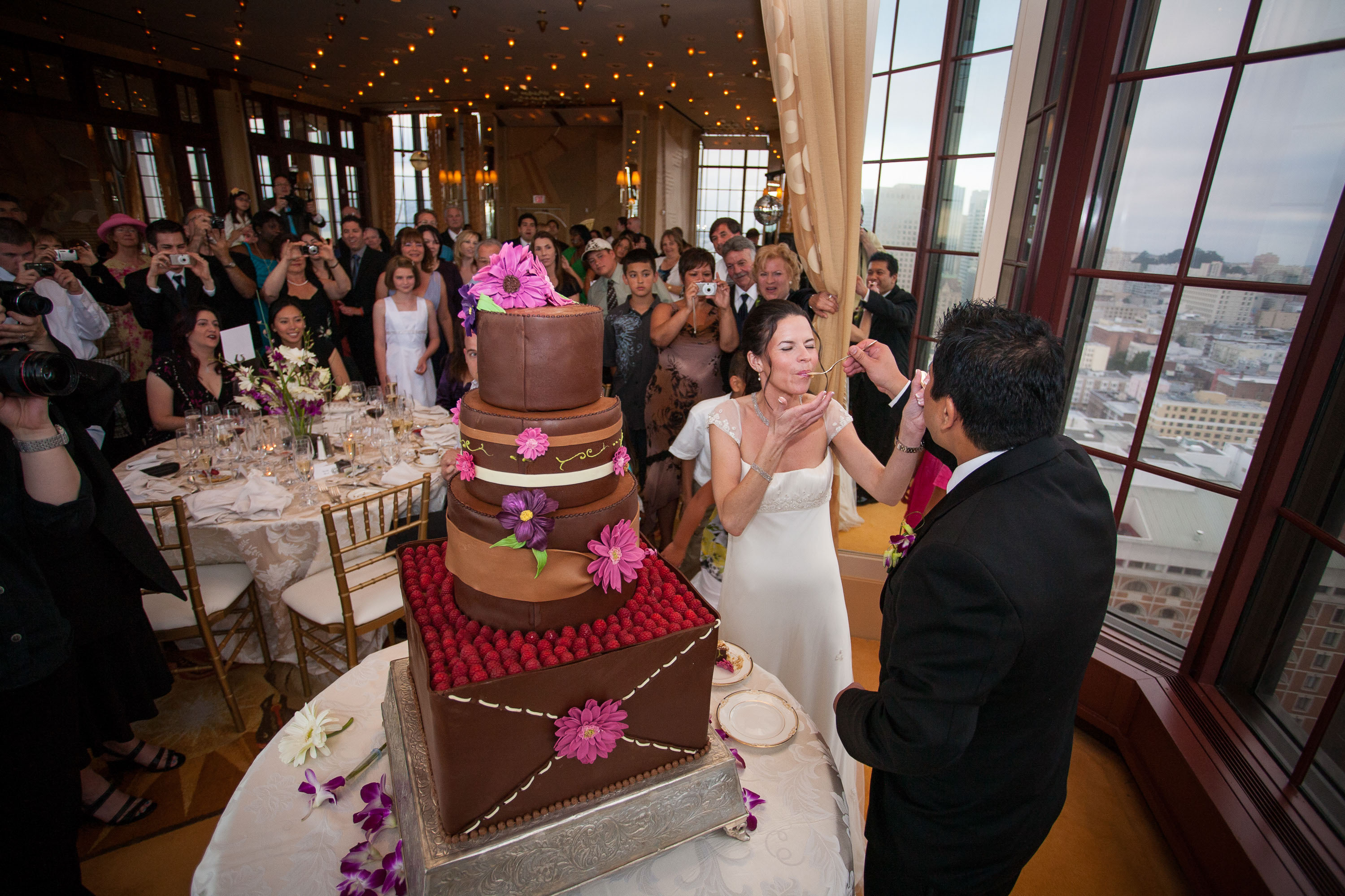 A panoramic view of the bride and groom sharing wedding cake, the assembled guests, and the incredible view from the St. Francis Hotel 