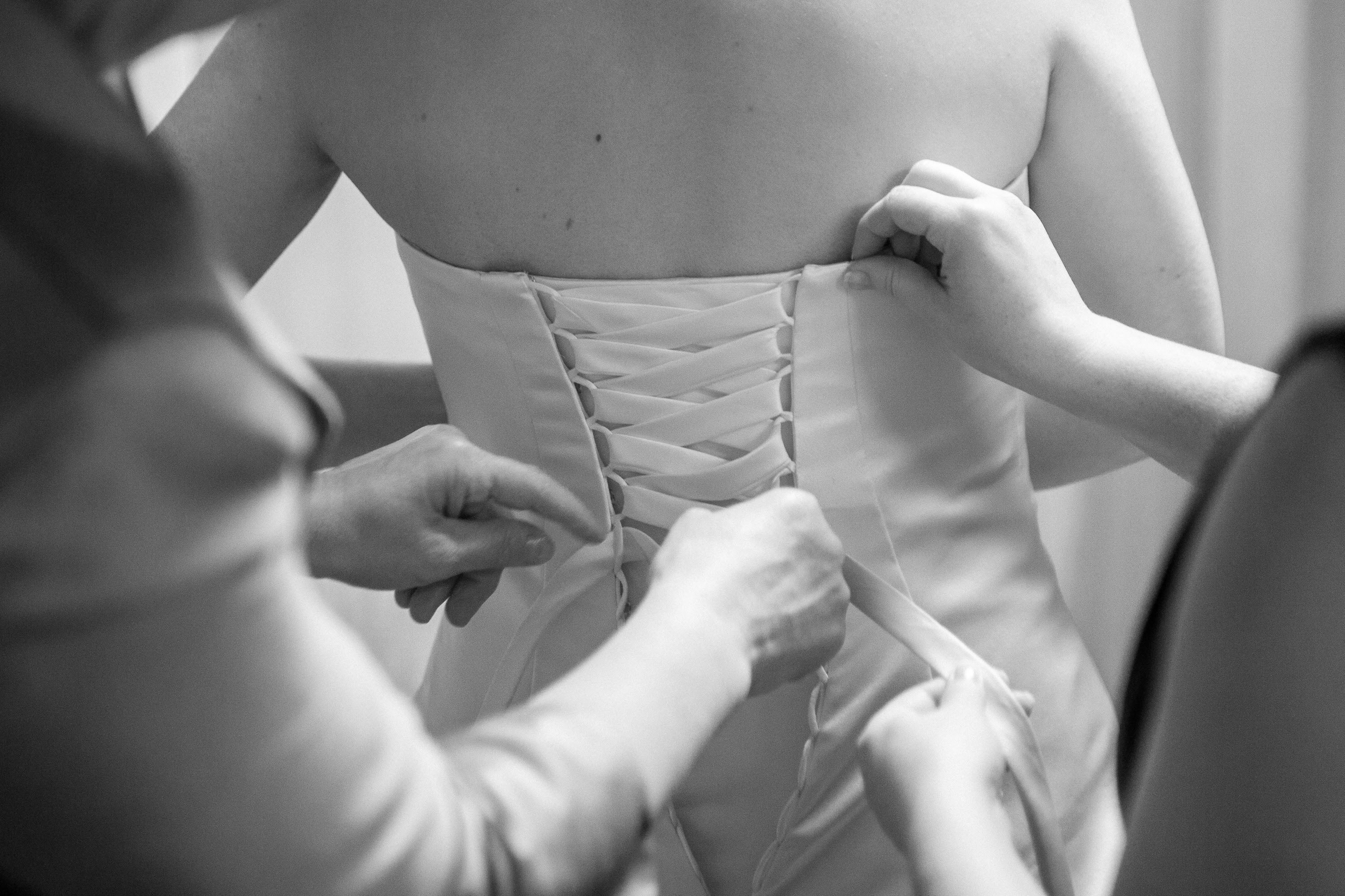 Bridesmaids lace up the ribboned back of a wedding dress, at St. Mary's Cathedral in San Francisco.